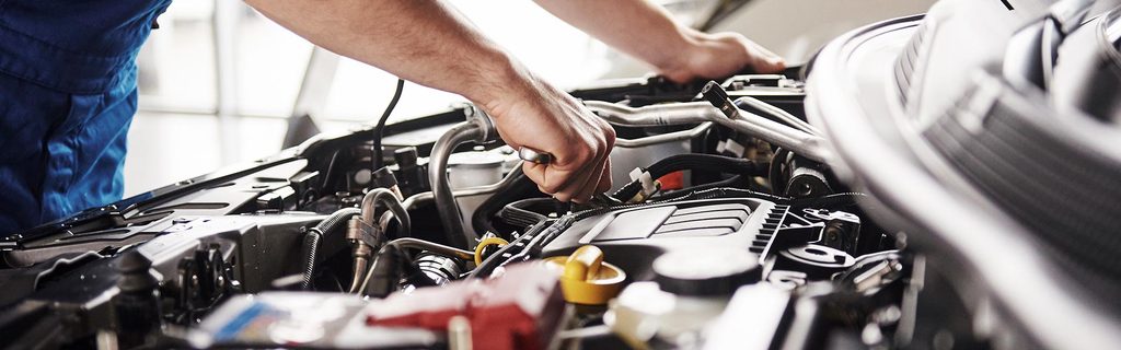 A close-up view of the hands of a  certified mechanic checking out an engine on a vehicle at a GMC Service Center