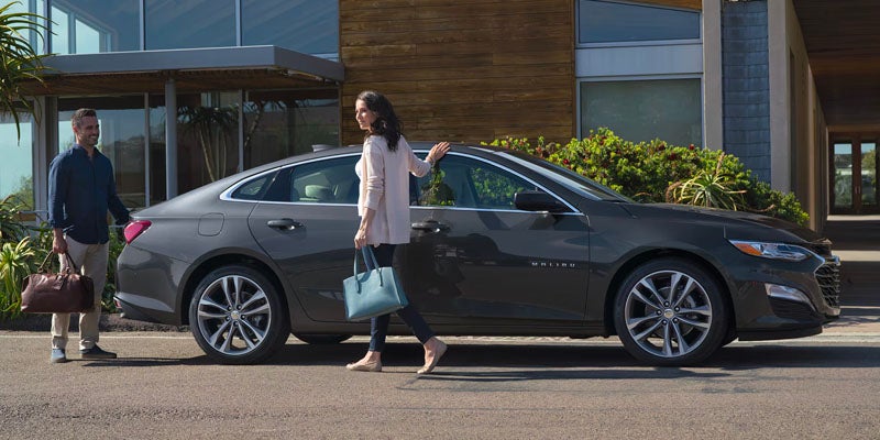 A women and men stands near Malibu car with bag